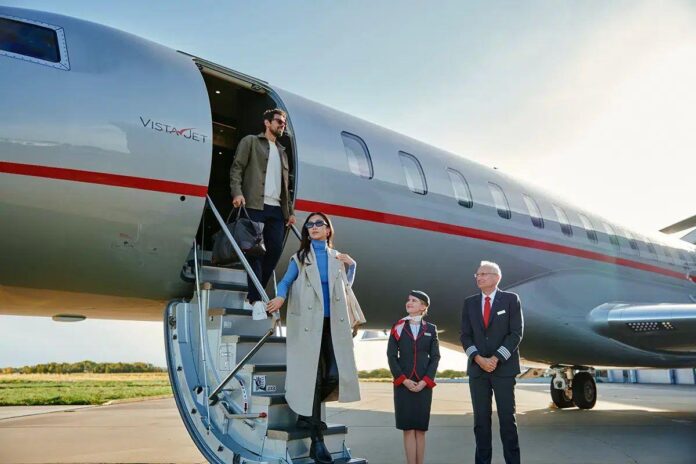 Aeronave prateada da VistaJet com detalhe em vermelho, passageiros se preparando para embarque, em um fundo de céu claro na pista do aeroporto.