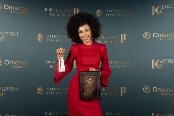 Evento de caridade TOP CHARITY com Omenaa Mensah, mulher com cabelo cacheado e vestido vermelho, segurando prêmios sob um fundo elegante com logotipos dourados.