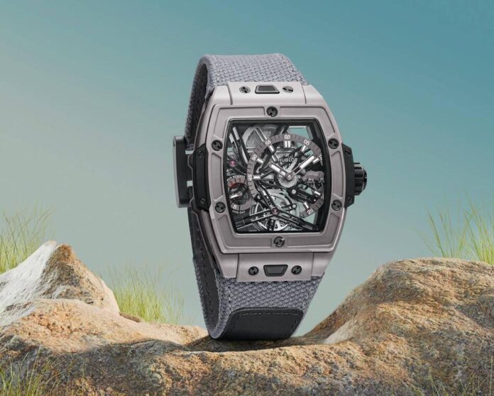Relógio Hublot Spirit of Big Bang, com caixa cinza e pulseira em tecido texturizado, em um fundo de céu azul e grama.