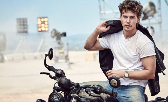 Um jovem vestindo uma roupa casual, com uma motocicleta em destaque e equipamentos de filmagem ao fundo, criando uma atmosfera vibrante e dinâmica.