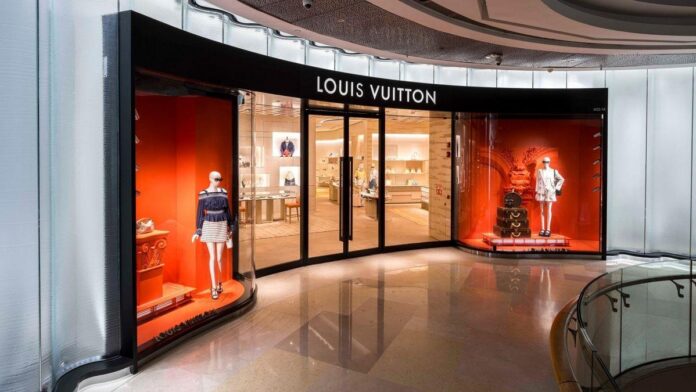 Uma loja da Louis Vuitton com fachada iluminada e produtos de luxo expostos em fundo interno.