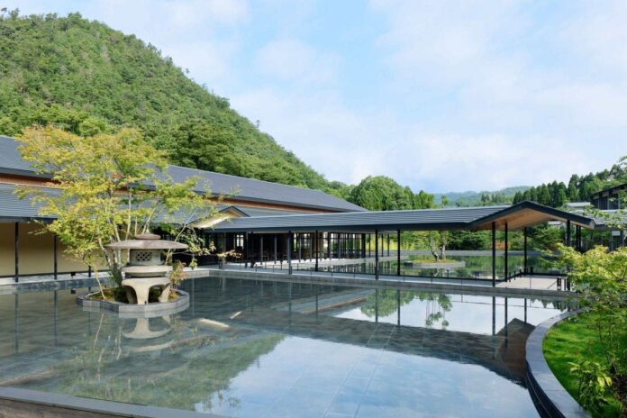 Bacia de água grande no pátio do hotel Roku Kyoto com reflexos das montanhas arborizadas ao fundo. A imagem transmite um ambiente moderno e integrado à natureza.