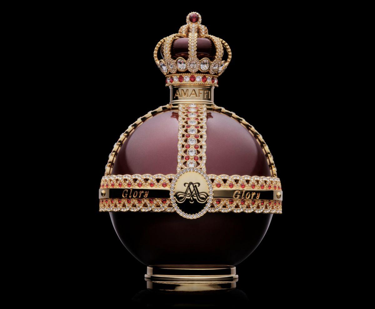 Frasco de perfume arredondado com tampa em forma de coroa sobre fundo preto, com detalhes em pedras preciosas.