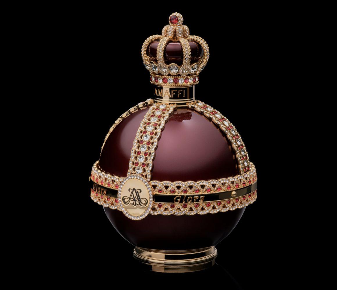 Frasco de perfume redondo com tampa de coroa em um fundo preto, com detalhes em pedras preciosas.