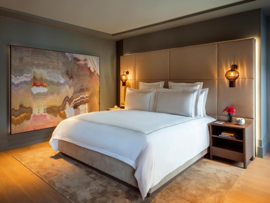 Um interior suave com uma cama grande, uma obra de arte na parede e flores na mesinha de cabeceira.