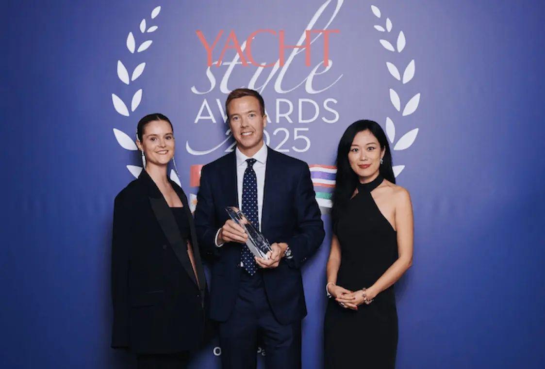 Um troféu sendo segurado por um homem em traje formal no Yacht Style Awards 2025, com logotipo do evento ao fundo e um ambiente decorado.