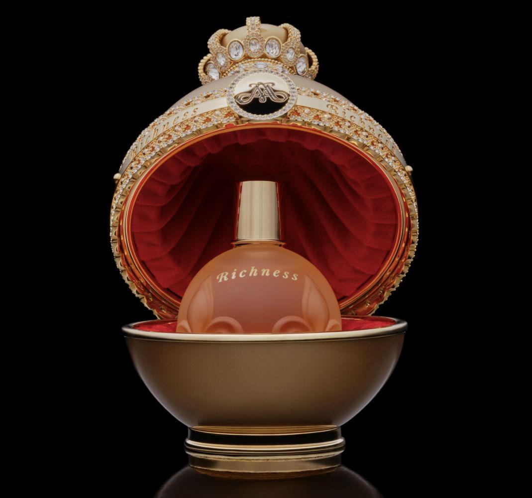Uma caixa luxuosa com frasco de perfume, decorada com pedras brilhantes e detalhes em veludo, em um fundo preto.