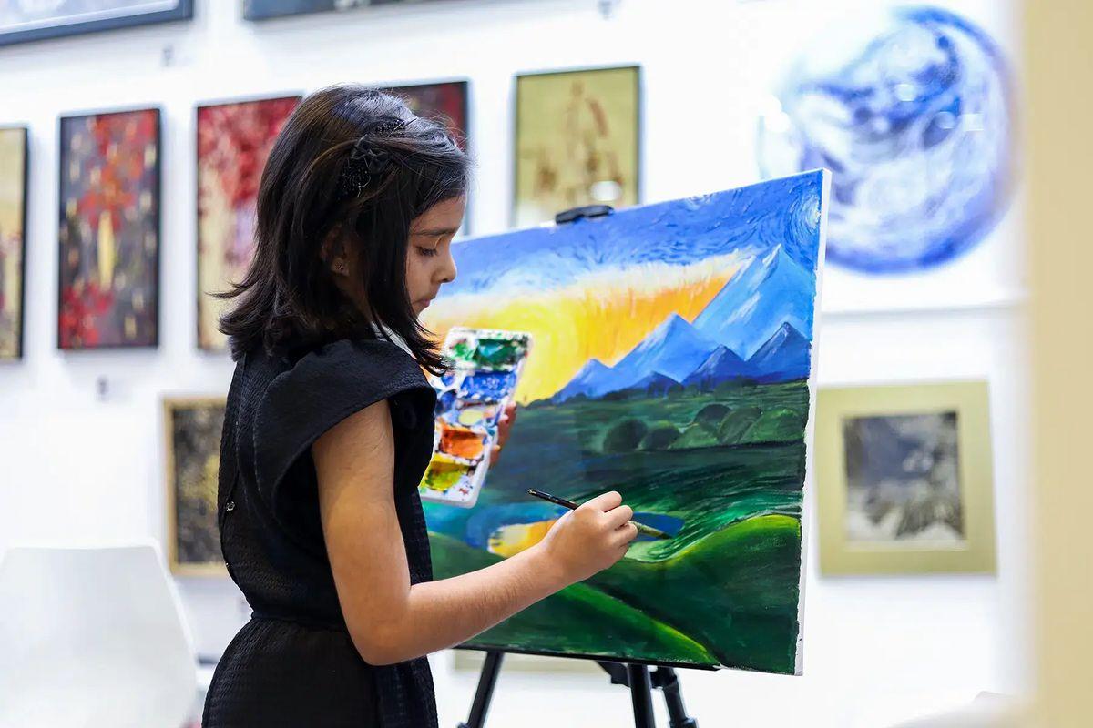 Uma galeria de arte com várias obras emolduradas e uma criança pintando com um pincel.